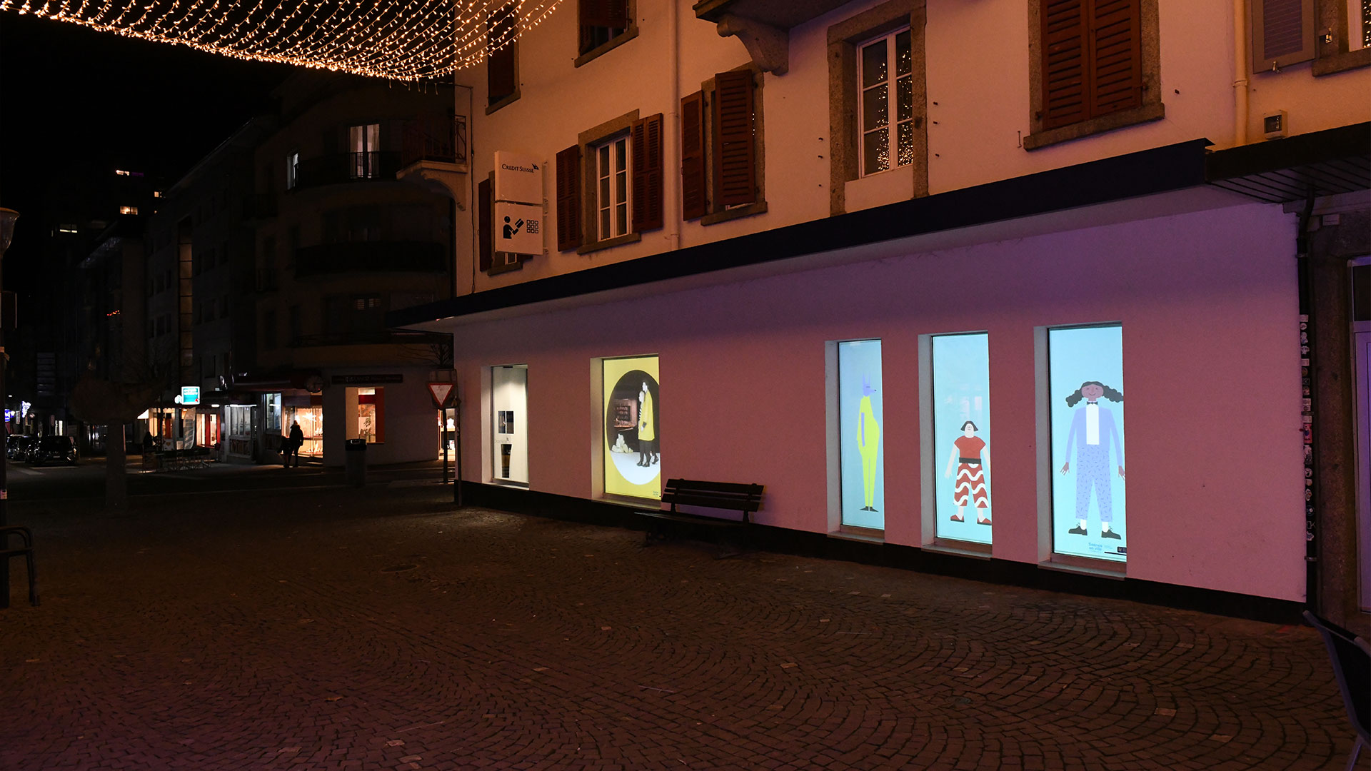 Rue à Monthey avec deux vitrines montrant des projections vidéos du projet Scènes en ville.