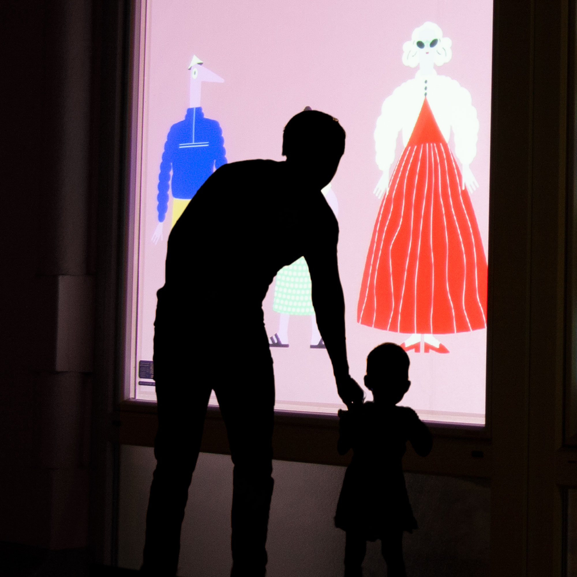 Un père et son fils regardent une projection animée sur une vitrine à Porrentruy. La vidéo montre des illustrations de personnages changeant de costumes.